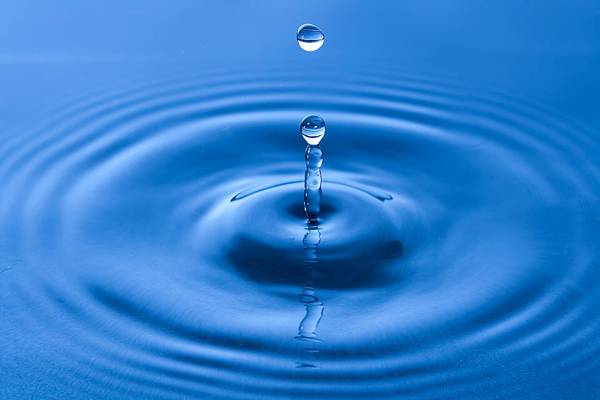 Gota de agua cristalina cayendo sobre una superficie azul